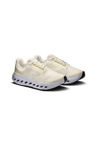 Zapatillas deportivas ligeras en malla crema y blanca, con un diseño estampado, cordones amarillos y una suela gruesa blanca con acentos negros.