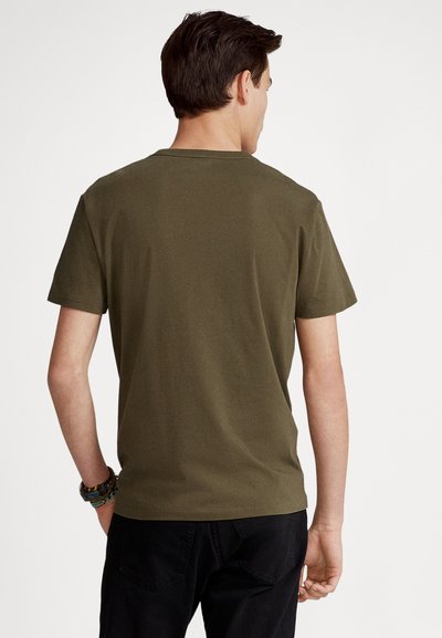 Olive green cotton t-shirt with short sleeves, crew neck, and a smooth texture, viewed from the back, paired with black pants.