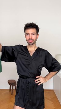 Sort satin morgenkåpe med korte ermer og midjebånd, med en glatt tekstur. Bakgrunnen inkluderer en lys vegg og tregulv.