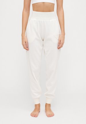 Pantaloni della tuta bianchi comodi con vita alta, polsini elasticizzati e un delicato dettaglio del logo in rilievo sul lato. Tessuto morbido.