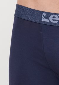 Marinblå herrboxershorts med ett texturerat elastiskt midjeband som har en ljusblå logotyp. Släta, figurnära tyger med minimala sömmar.