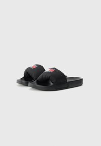 Sandales à glissière noires rembourrées avec des bretelles larges et une semelle en caoutchouc lisse. Présente un petit logo rectangulaire avec des accents rouges et bleus sur la bretelle.