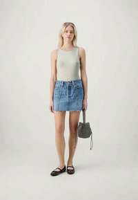 Top sem mangas cinza claro, saia mini de ganga azul com barra desfiada e sapatos planos pretos. Os acessórios incluem uma pequena bolsa preta com padrão.