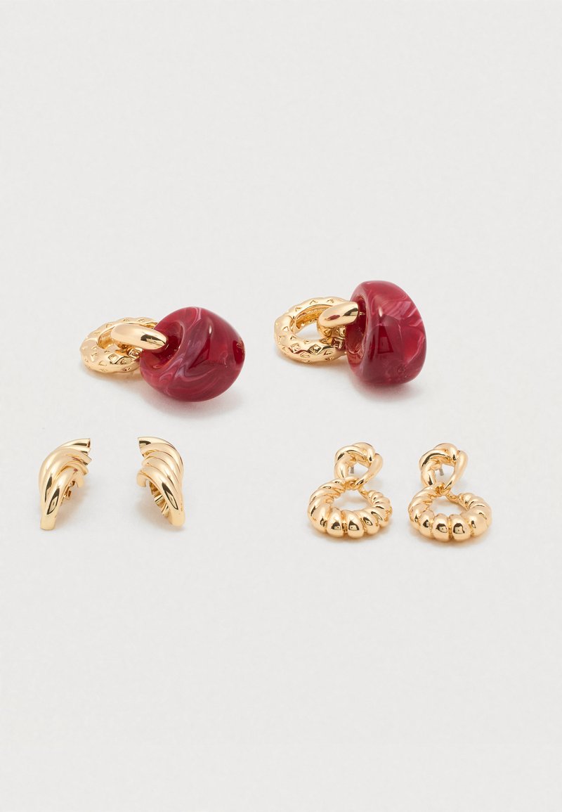 Uhani v zlato barvi z rdečimi marmoriranimi kroglicami in teksturiranimi obročki. Vključuje dva stila: ukrivljene oblike in poudarek z okrasno kroglico, vsi s sijočim zaključkom.