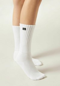 White ribbed socks with a folded cuff, featuring a small black label with "clz" on the outer side. Smooth texture, ankle-length design.