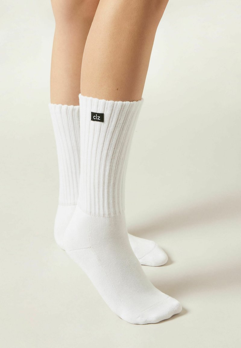 White ribbed socks with a folded cuff, featuring a small black label with "clz" on the outer side. Smooth texture, ankle-length design.