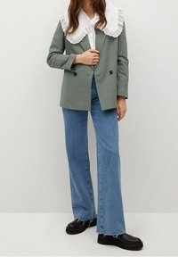 Blazer de cuadros verdes y blancos, cruzado, con un gran cuello de encaje blanco, combinado con vaqueros acampanados azules y zapatos de plataforma negros.