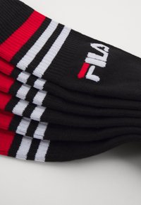 Calcetines negros con rayas horizontales rojas y blancas y un logo de Fila. La tela es suave, con una textura elástica y un diseño atlético clásico.