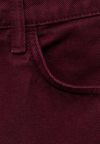 Gros plan sur un tissu en denim rouge foncé montrant une boucle de ceinture et le bord supérieur d'une poche avant avec des coutures visibles.