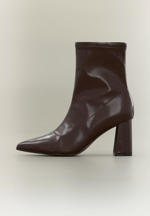 Bottine en cuir marron foncé avec bout pointu et talon bloc sur un fond neutre.