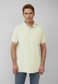 Bleke gele polo shirt met een klassiek ontwerp, korte mouwen en een knoopsluiting met drie knopen. De stof heeft een subtiele textuur. Draagt met blauwe jeans.