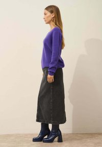 Fioletowy sweter z dzianiny, czarna jeansowa spódnica maxi i niebieskie lakierowane trzewiki na platformie. Strój charakteryzuje się luźnym krojem i miękkimi teksturami.