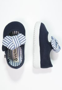 Zapatos de lona en color marino con un lazo a rayas, suela de goma blanca y forro interior a rayas. Diseño tipo slip-on con puntera redondeada.