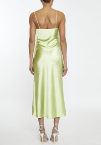 Abito midi in satin verde chiaro, caratterizzato da sottili spalline e una silhouette aderente. Texture liscia con una leggera lucentezza e spacco posteriore.