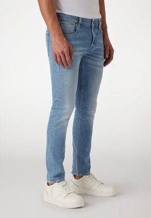 Jeans skinny de denim azul claro con detalles desgastados, cinco bolsillos y una cintura de corte medio. Combinados con zapatillas blancas para un contraste.