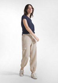 Granatowy top z krótkim rękawem, zestawiony z beżowymi spodniami typu cargo z elastycznymi mankietami. Spodnie posiadają boczne kieszenie. Stylizacja uzupełniona jasnymi sneakersami.