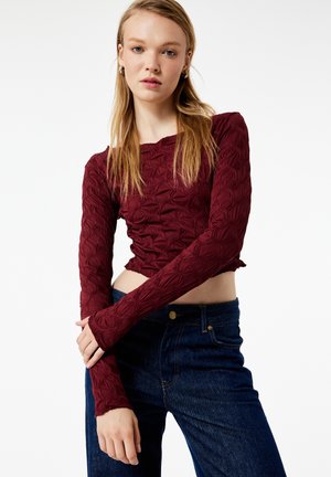 Bordeaux gekruist langekolen crop top met een textuurpatroon. Combinatie met hooggetailleerde donkerblauwe jeans met een klassieke knop en zakken.