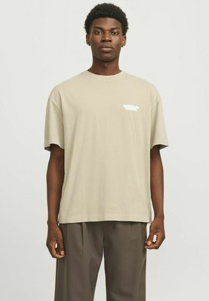 T-shirt en coton beige à coupe décontractée, à manches courtes, avec du texte imprimé blanc sur la poitrine. Assorti à un pantalon large marron foncé.