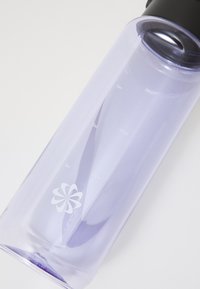 Bouteille d'eau en plastique transparent violet avec un couvercle noir, présentant des graduations et un logo floral blanc sur le côté.