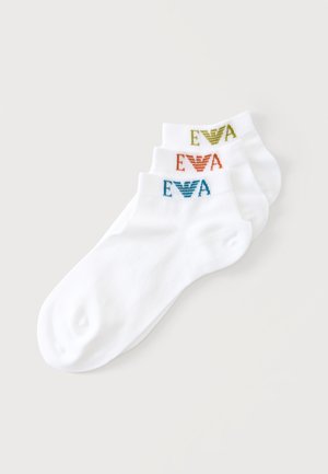 Trois paires de chaussettes blanches chevilles empilées, chacune avec un logo "EVA" coloré et un dessin d'aigle près du bord en bleu, orange et vert.