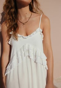 Robe blanche avec des accents froncés au niveau du col et de l'ourlet. Bretelles spaghetti réglables, tissu léger, texture lisse.