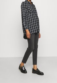 Svart och vit rutad långärmad skjorta med två bröstfickor, matchad med mörkgrå slim-fit jeans och svarta mockasiner med en glänsande spänne.