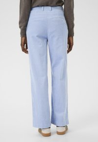 Lichte blauwe wijde corduroy broek met verticale ribbeltextuur; heeft achterzakken en een gladde tailleband; gecombineerd met casual schoenen.
