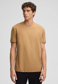 Korte mouwen, ronde hals t-shirt in lichtbruin katoen, met een gladde textuur en eenvoudig ontwerp, gecombineerd met donkere broeken.
