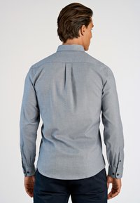 Grijze, langarm shirt met een getailleerde pasvorm, rugplooien en knoopmanchetten. Glad stof met een subtiele textuur.