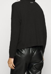 Pull noir court avec col roulé côtelé et bordure contrastée, fabriqué en matière tricotée douce. Dos uni avec détail du logo au niveau du cou.