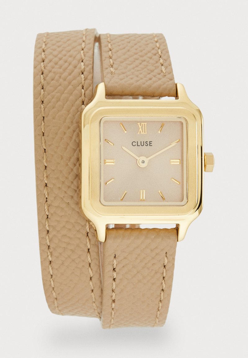 Montre carrée dorée avec un bracelet en cuir texturé beige, arborant un cadran minimaliste avec des chiffres romains et des aiguilles fines.