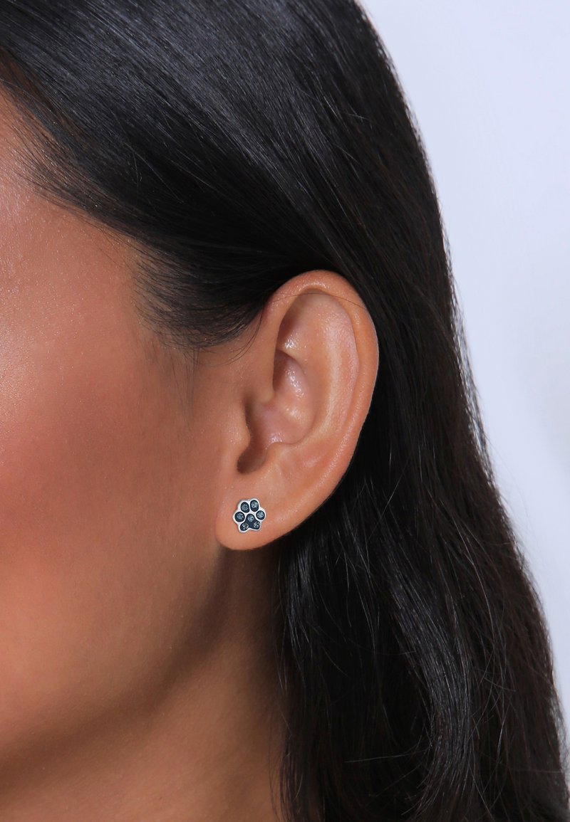 Boucles d'oreilles en argent sterling en forme d'empreinte de patte, avec des accents bleu foncé et un fini poli, portées sur un lobe d'oreille.