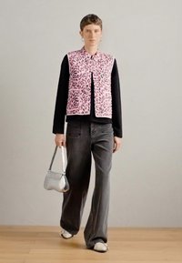 Κοντό γιλέκο με λεοπάρ μοτίβο σε ροζ απόχρωση πάνω από μαύρο πουκάμισο με μακρύ μανίκι, συνδυασμένο με γκρίζες παντελόνες σε φαρδιά γραμμή και ασημένια τσάντα.