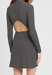 Mustavalkoraidallinen mekko, jossa on korkea kaula-aukko, pitkät hihat ja leikattu selkäosa, jolloin se on tiukka yläosasta ja hulmuava hame.