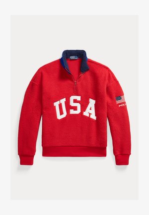 Czerwony pulower z polaru z granatowym kołnierzem, białymi literami "USA" na przodzie oraz naszywką z flagą Stanów Zjednoczonych i napisem "Polo" na lewym rękawie.
