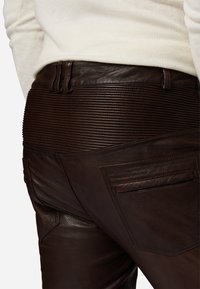 Bruine leren broeken met een geribbeld tailleband, achterzakdetails en een gladde textuur, met een op maat gemaakte pasvorm en ontwerp elementen.