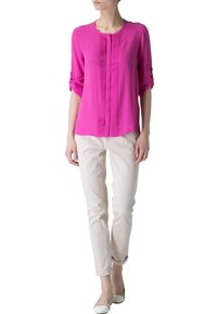 Blouse fuchsia avec plis, col rond et manches retroussées, associée à un pantalon slim crème et des ballerines neutres.