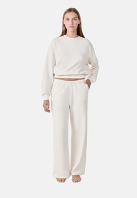 Cremfarbener Loungewear-Set aus weichem Stoff, bestehend aus einem verkürzten Sweatshirt und lockeren Hosen mit elastischem Bund und Taschen.