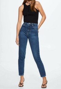 Hochtaillierte blaue Jeans mit schmalem Schnitt, umgeschlagenen Säumen und Fünf-Taschen-Design, kombiniert mit einem ärmellosen schwarzen Top.