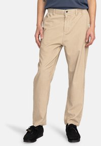 Beige corduroy pants with a straight fit, textured fabric, front button closure, and side pockets, paired with black shoes.