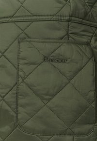 Πράσινο επενδυμένο μπουφάν με μεγάλη τσέπη στο στήθος και διακριτό κεντημένο λογότυπο. Μαλακό υλικό με λεπτομέρειες ραφής σε σχέδιο διαμαντιού.