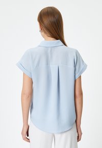 Lyseblå kortærmet skjorte med spredt krave, rygstykke og rundet kant. Stoffet ser blødt ud med en subtil tekstur.