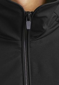 Schwarze Jacke mit hohem Kragen, Frontreißverschluss und glatter Textur. Verfügt über einen haltbaren Reißverschluss mit matter Oberfläche, entworfen zum Schichten.