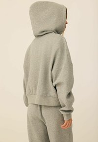 Szara bluza z kapturem wykonana z miękkiego materiału, charakteryzująca się luźnym krojem, ściągaczami przy mankietach oraz rozciętym dołem. W zestawie z dopasowanymi szarymi spodniami.