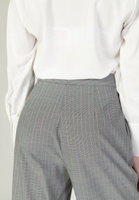 Pantaloni grigi a righe con accenti rosa chiaro, a vita alta e una vestibilità sartoriale, abbinati a una camicia bianca a maniche lunghe.