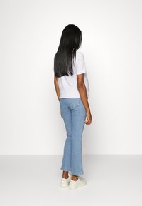 T-shirt cinza e branco às riscas, combinado com jeans flare azul claro e ténis brancos. Cabelo longo e liso, fotografado de costas.