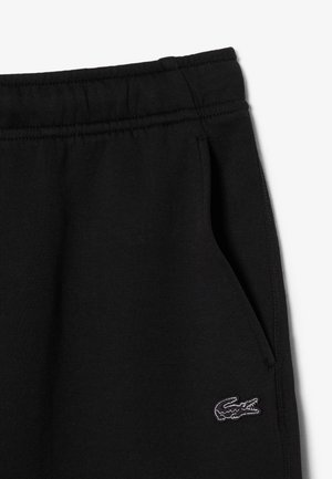 Zwarte joggingbroek met elastische tailleband, zijzak en klein geborduurd wit-zwart krokodillenlogo vlak bij de zak.