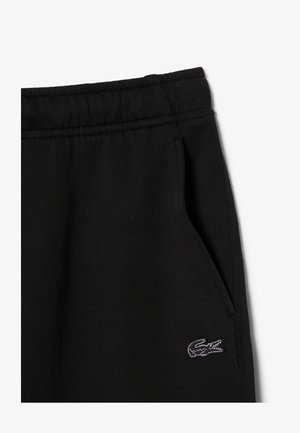 Zwarte joggingbroek met elastische tailleband, zijzak en klein geborduurd wit-zwart krokodillenlogo vlak bij de zak.