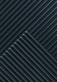 Gros plan sur des tapis en caoutchouc sombre s'entrecroisant, avec des crêtes parallèles surélevées formant un motif diagonal géométrique.