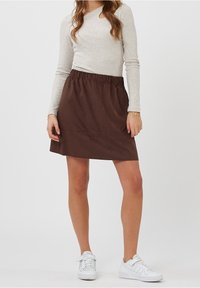 Gonna elasticizzata marrone realizzata in tessuto morbido, con un design semplice. Abbinata a una maglietta a maniche lunghe grigia chiara e scarpe da ginnastica bianche.